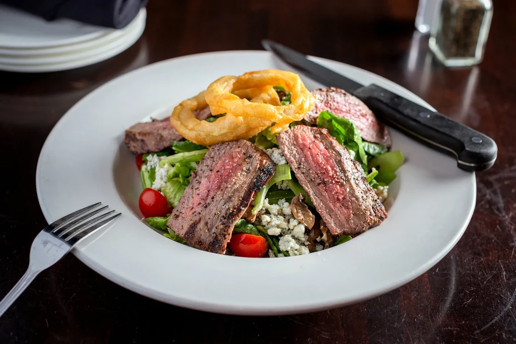 Steak salad with blue cheese, cherry tomatoes, and onion rings.