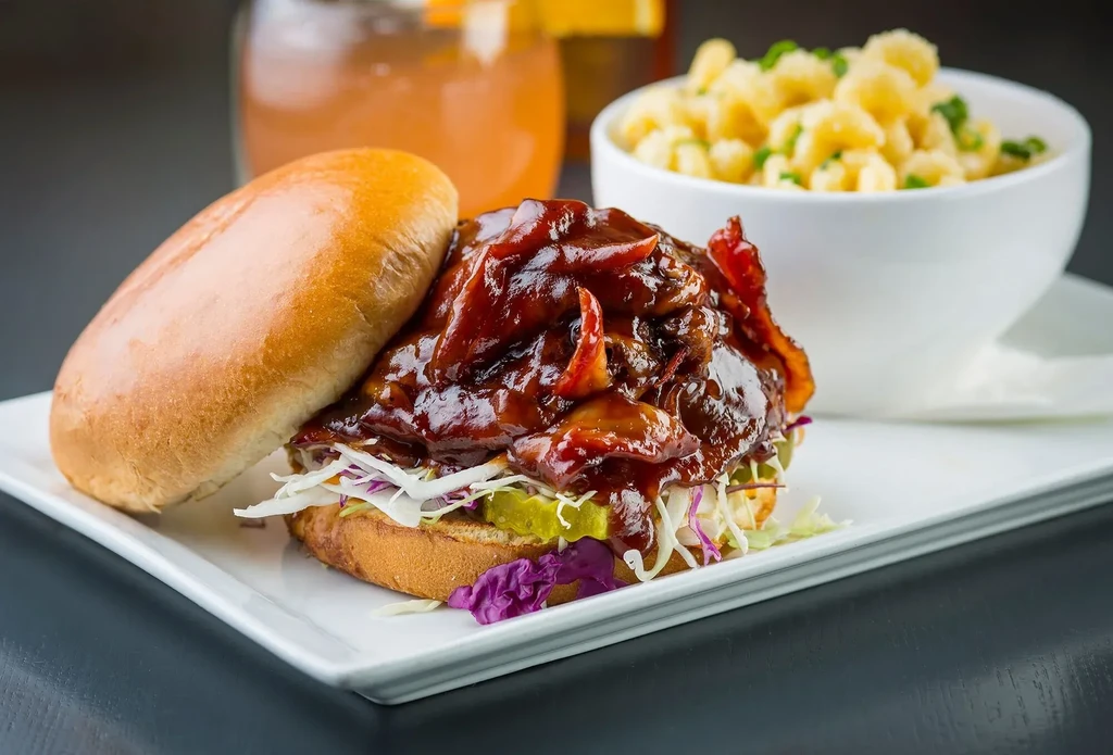 Open-faced BBQ pulled pork sandwich with slaw, bacon, and pasta.