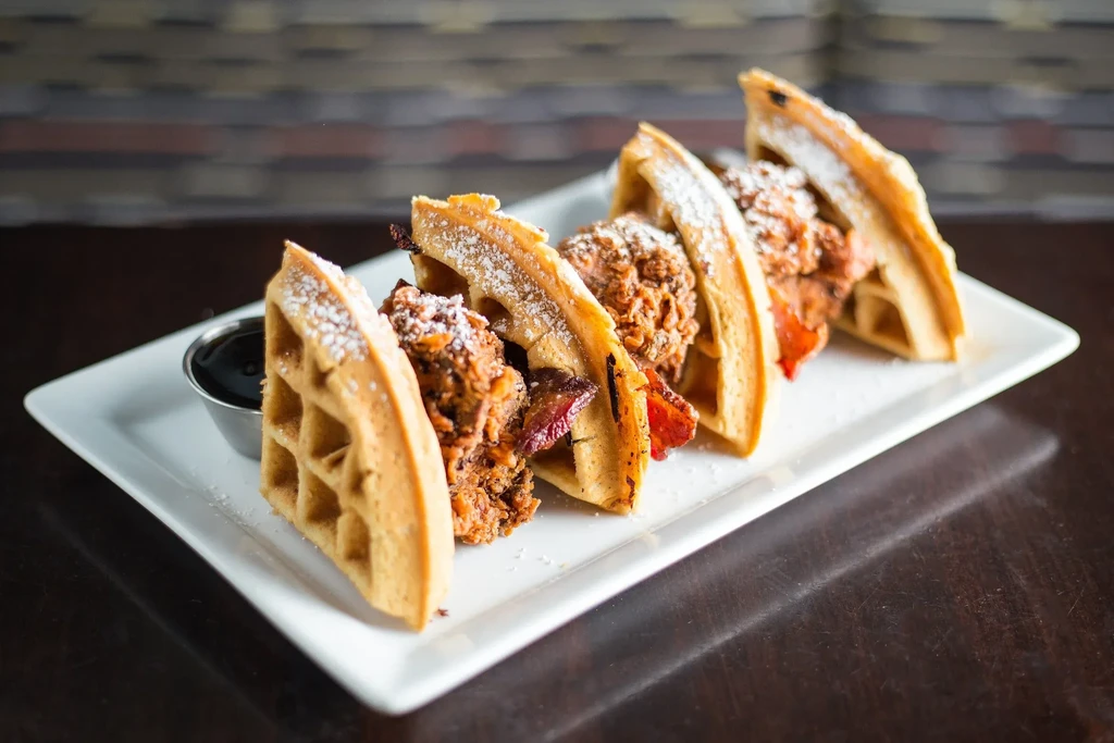 Four chicken and waffle tacos with bacon and powdered sugar.
