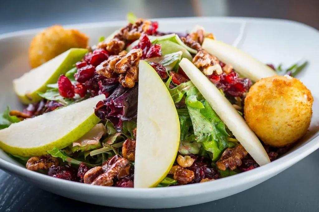 Salad with lettuce, walnuts, cranberries, pear, and fried items.