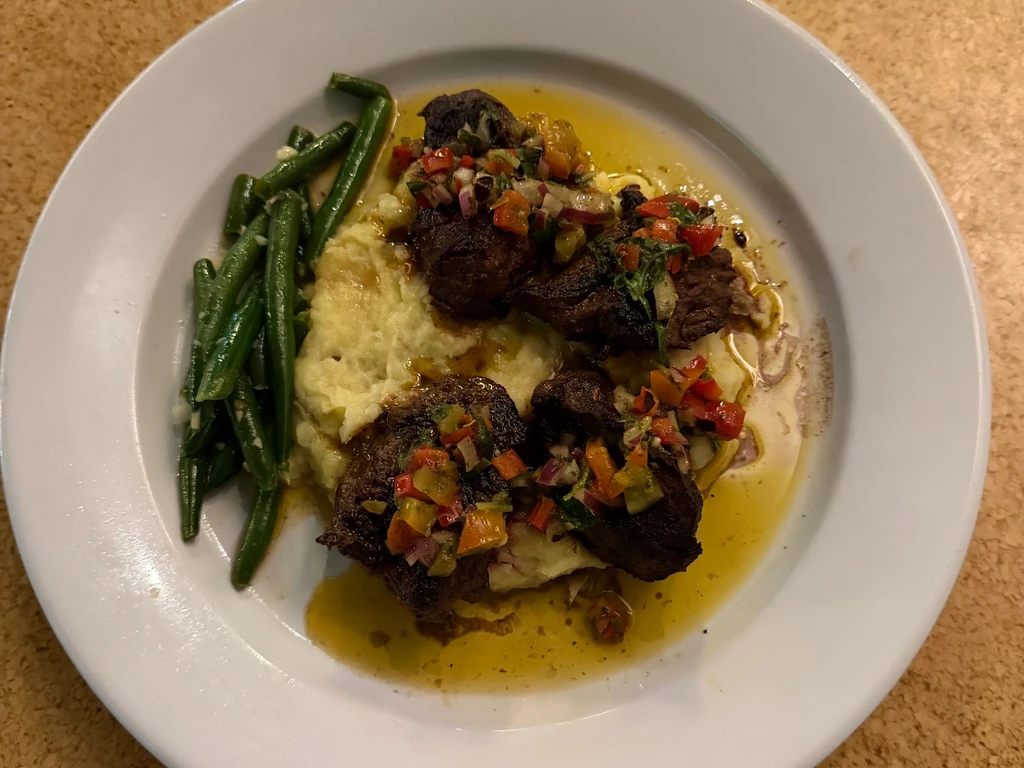 Plated meal with meat, mashed potatoes, green beans, and sauce.