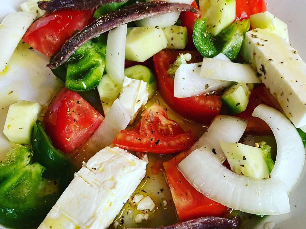 Overhead view of a colorful salad with tomatoes, peppers, onions, and feta.