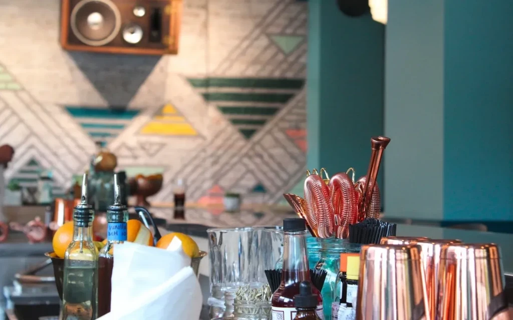 Bartending tools, oranges, and bottles on a bar counter.