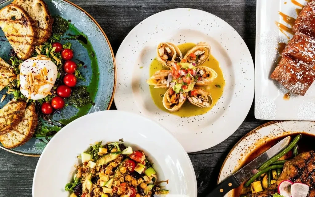 Flat lay of five distinct gourmet dishes on a dark table.