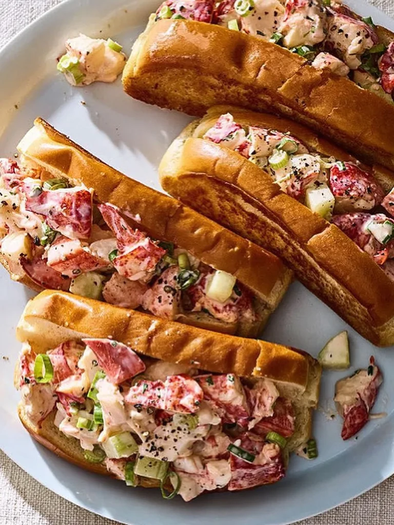 Four lobster rolls with creamy filling on a light platter.
