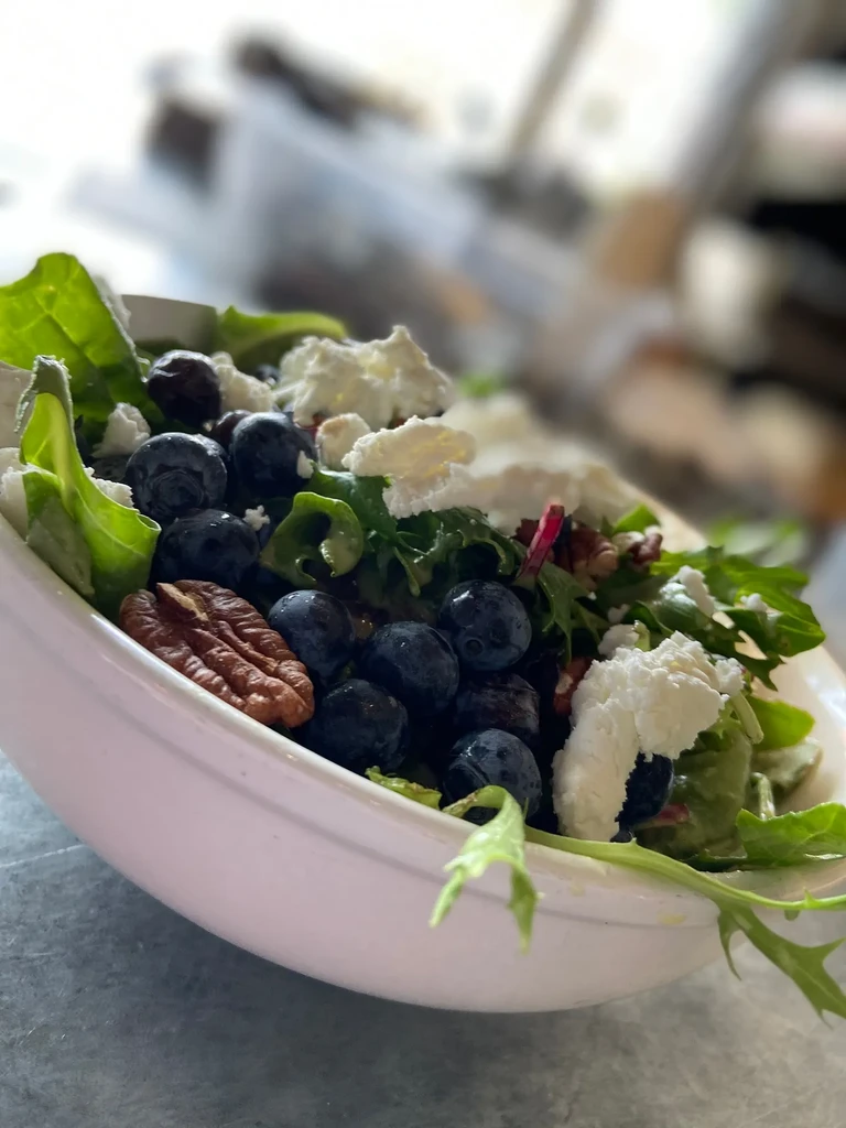 Close-up of a salad with greens, blueberries, cheese, and a pecan.