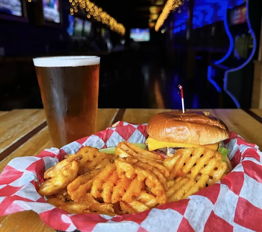 Burger, waffle fries, and beer in a dim restaurant setting.
