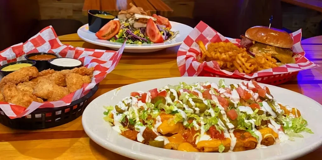 A wooden table spread with nachos, fried chicken, a burger, and salad.