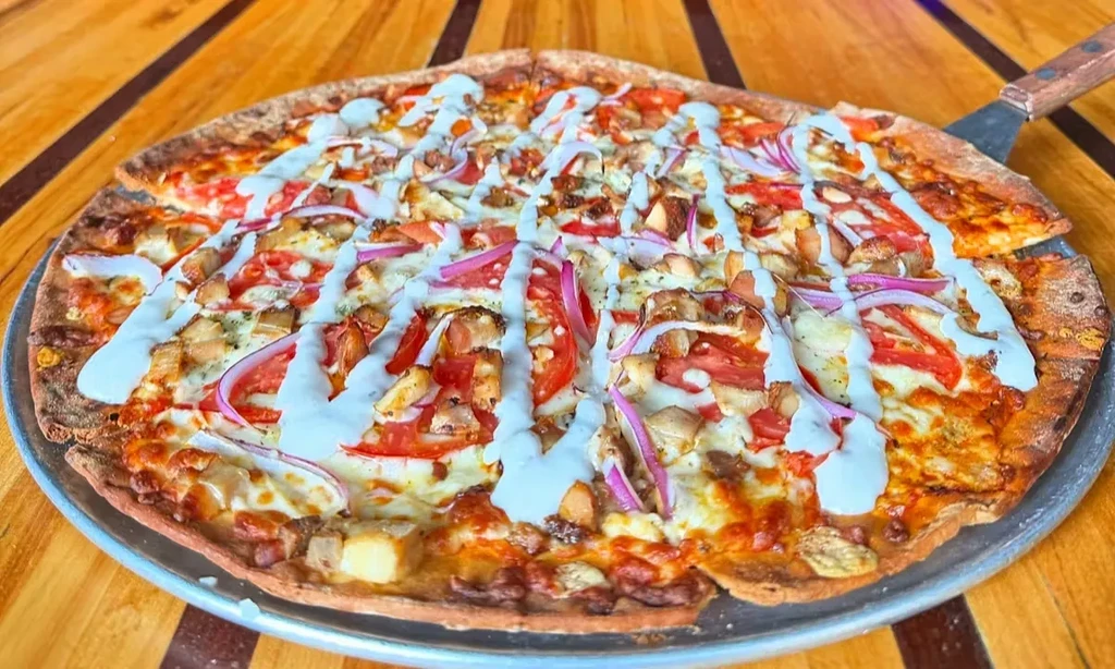 Round pizza with chicken, vegetables, and creamy sauce on a wooden table.