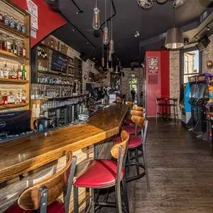 Empty bar interior with stools, bottles, and arcade games.