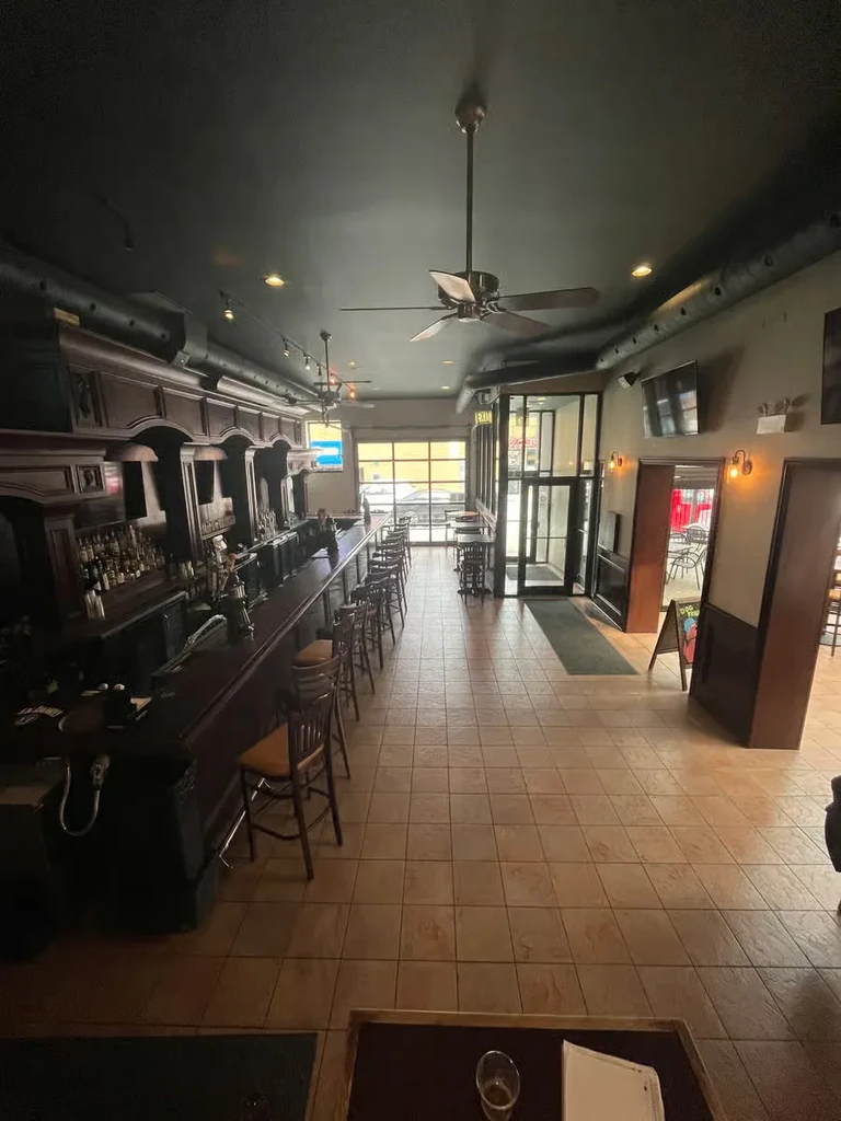 Restaurant interior with a long wooden bar, stools, and ceiling fans.