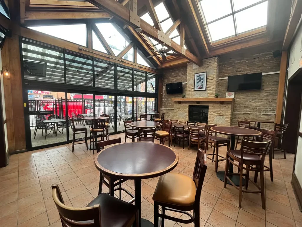 Restaurant interior with vaulted ceiling, fireplace, and outdoor patio view.