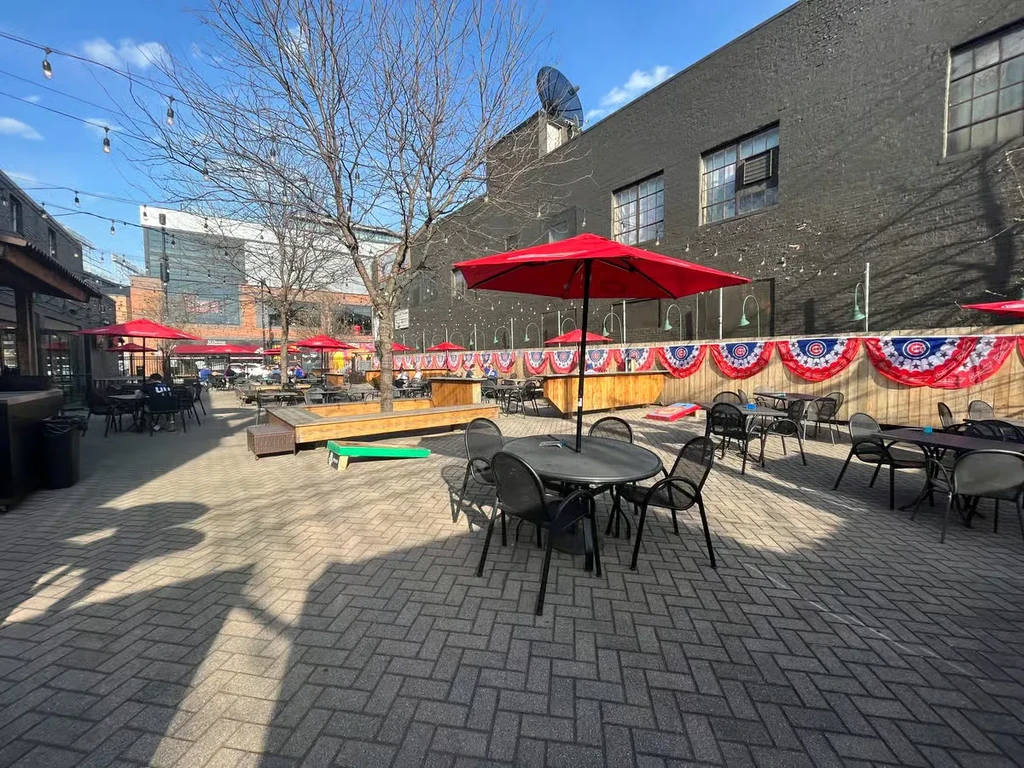 Outdoor restaurant patio with tables, red umbrellas, and festive bunting.