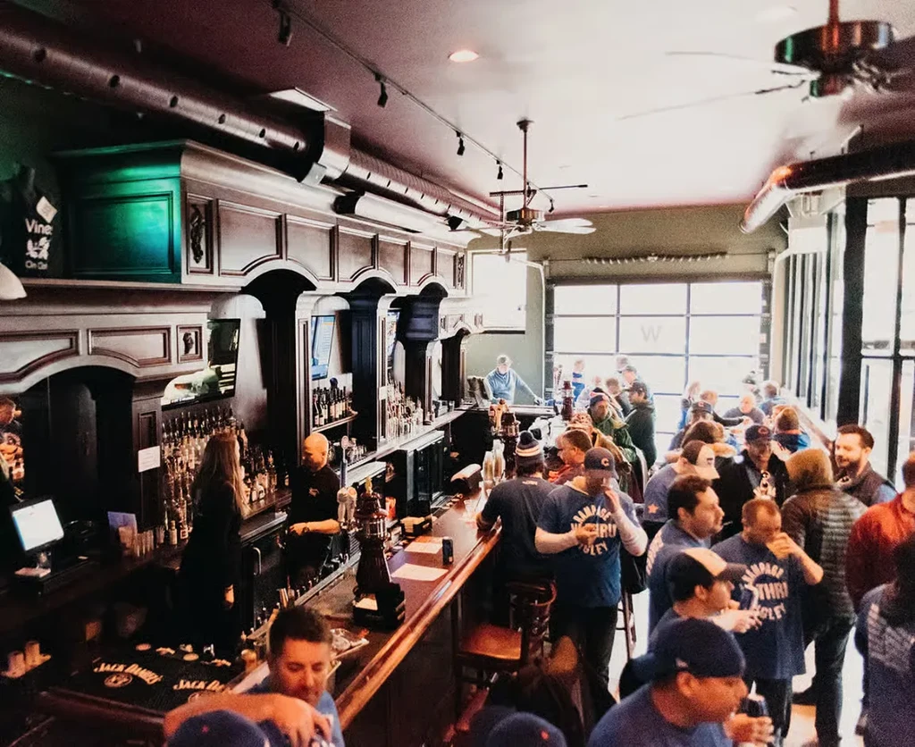 A bustling bar with many customers and two bartenders working.