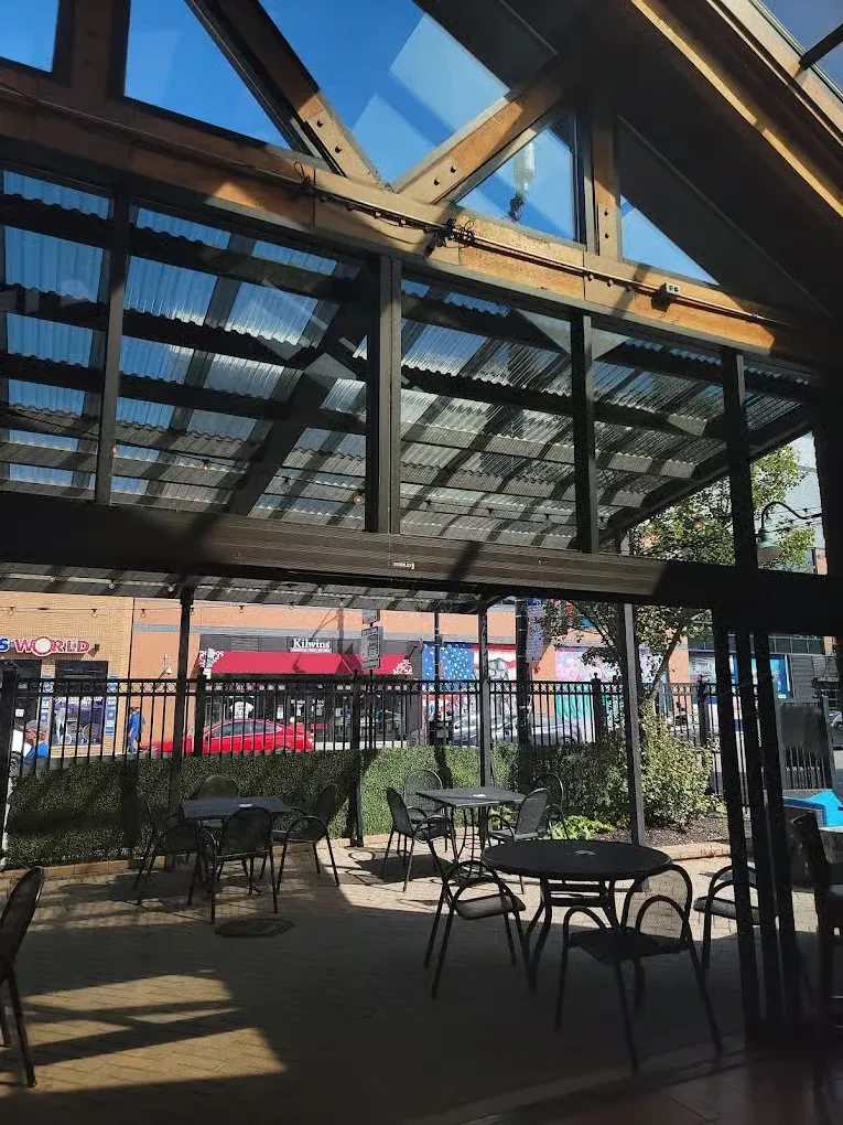 Outdoor patio with black tables, chairs, exposed beams, and street view.