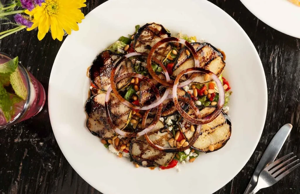 Grilled vegetable salad with cheese, pine nuts, and balsamic glaze.