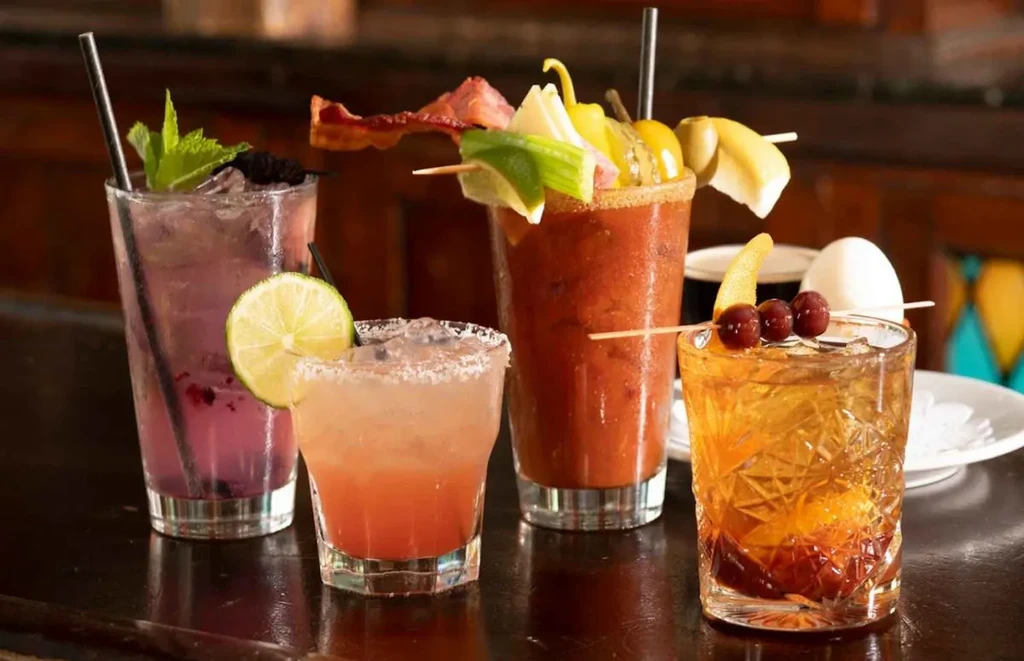 Four distinct cocktails with various garnishes on a dark surface.