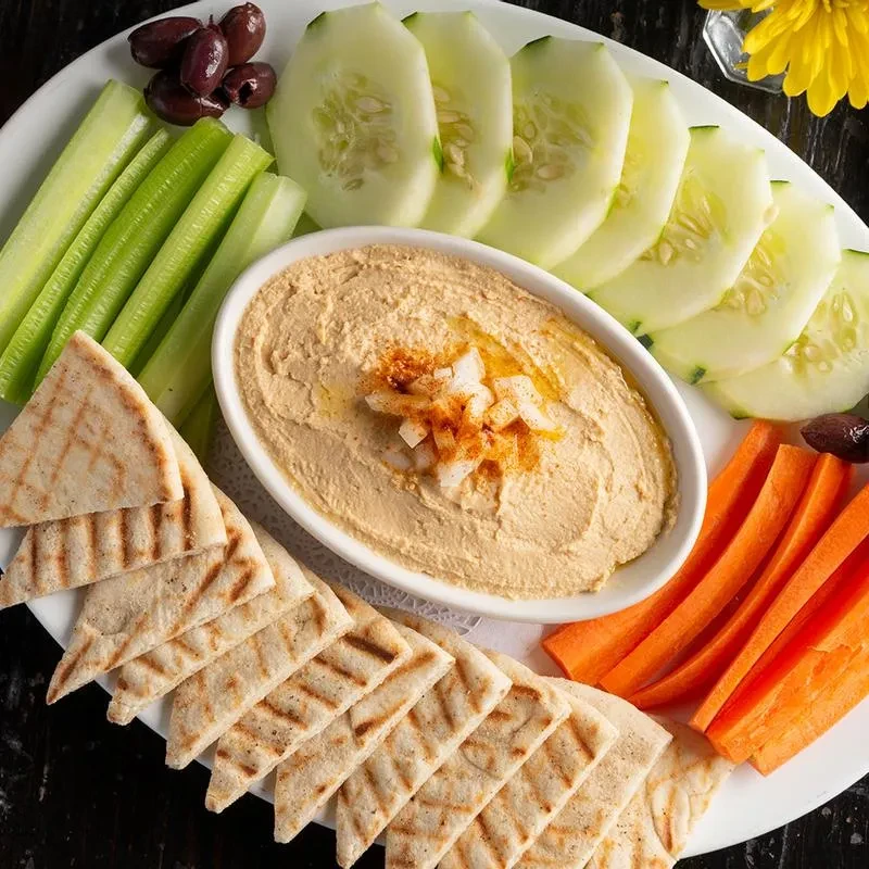 Hummus appetizer with vegetables and pita bread on a white platter.