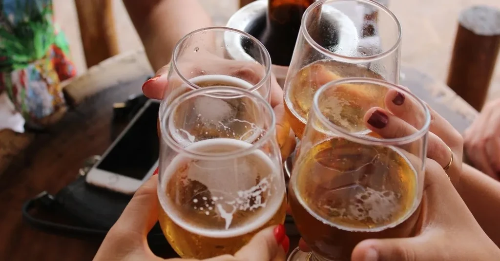 Group of people toasting with beer in stemless glasses.