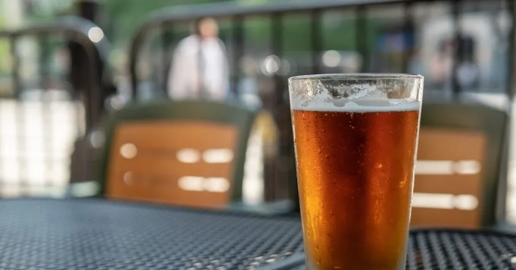 Glass of amber beer with foam and condensation on a table.