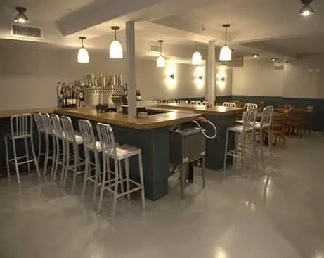 Modern bar interior with metallic stools, beer taps, and pendant lights.