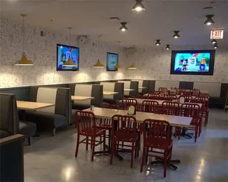 Empty restaurant with booths, tables, chairs, and wall-mounted TVs.