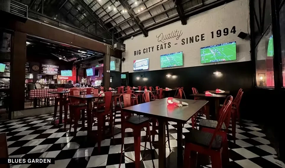 Restaurant interior with checkerboard floor, red chairs, and multiple TVs.
