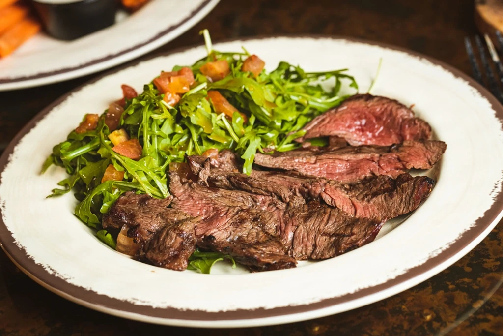 Close-up of sliced steak, salad, and a rustic plate.