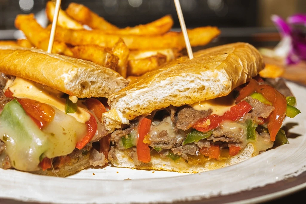 Philly cheesesteak sandwich with peppers, cheese, and fries on a plate.