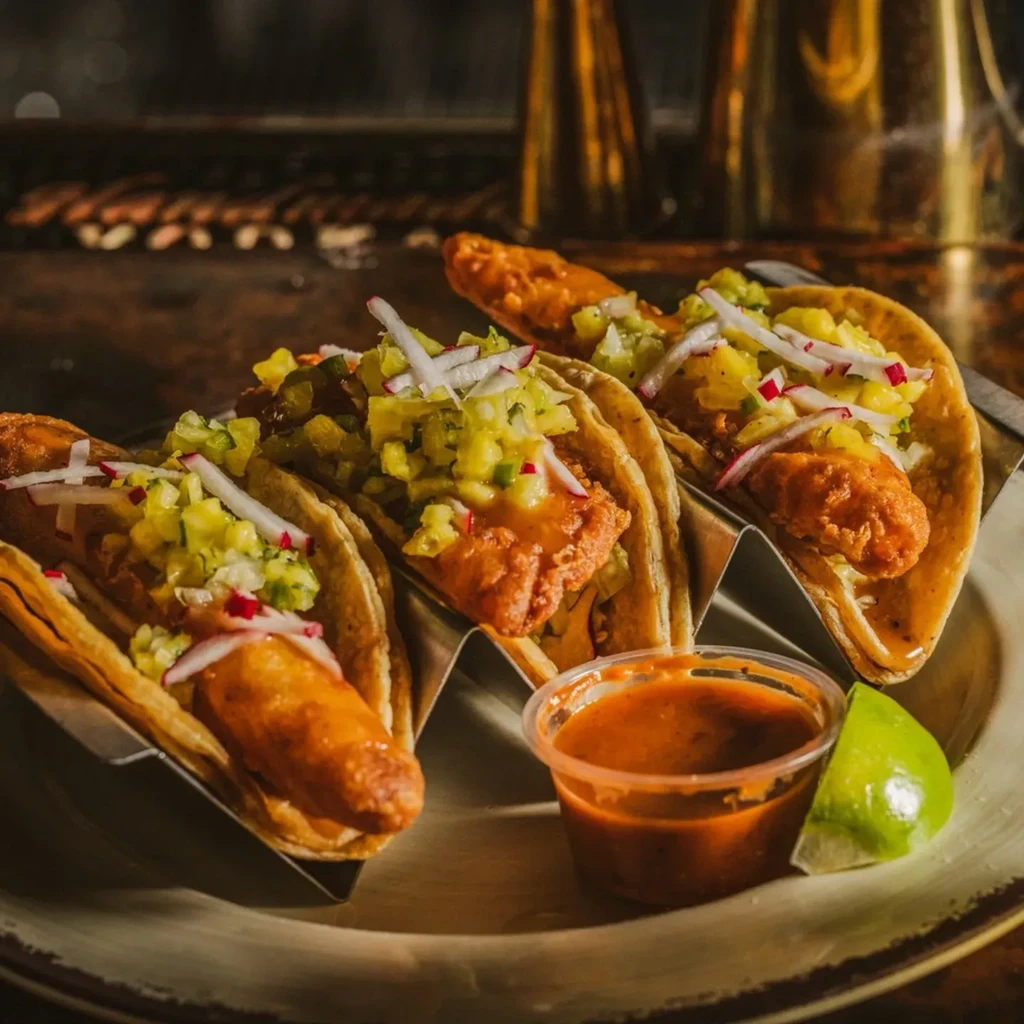 Three fried tacos with fruit salsa and radishes, sauce, and lime.
