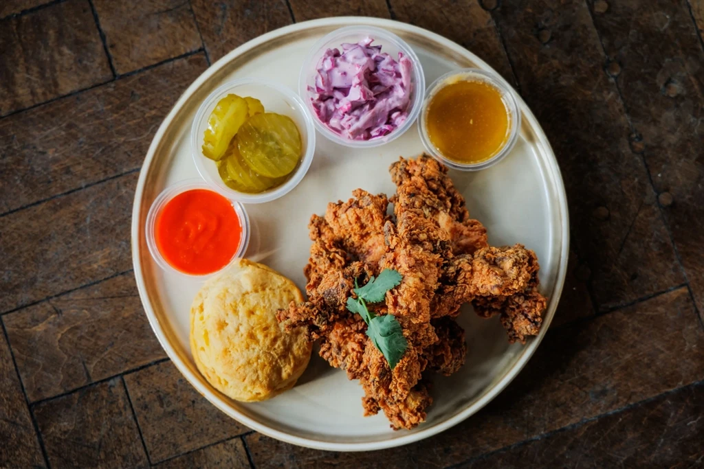 Fried chicken meal with sides, biscuit, and sauces on a plate.