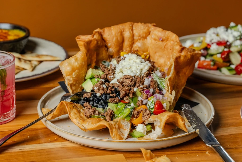 Taco salad in a crispy fried tortilla bowl with various toppings.