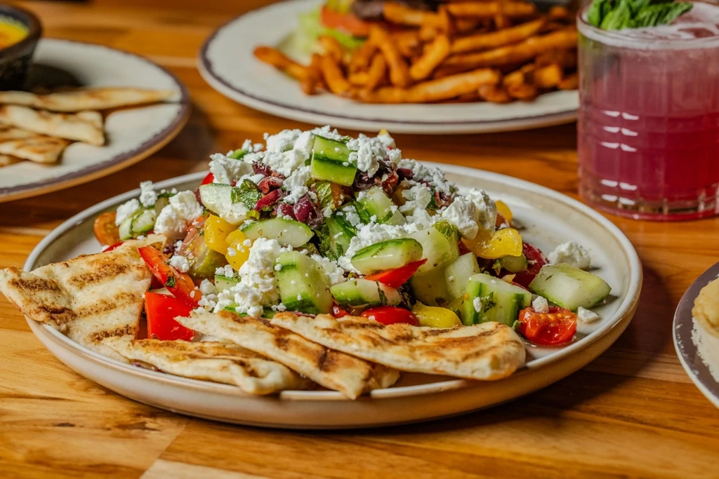 Colorful salad with flatbread, fries, and a pink drink on a wooden table.