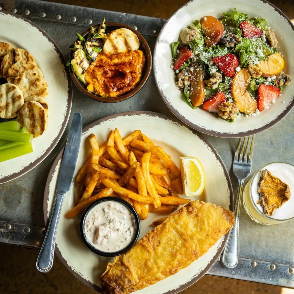 Flat lay of fried fish, fries, pita, salad, and a drink.