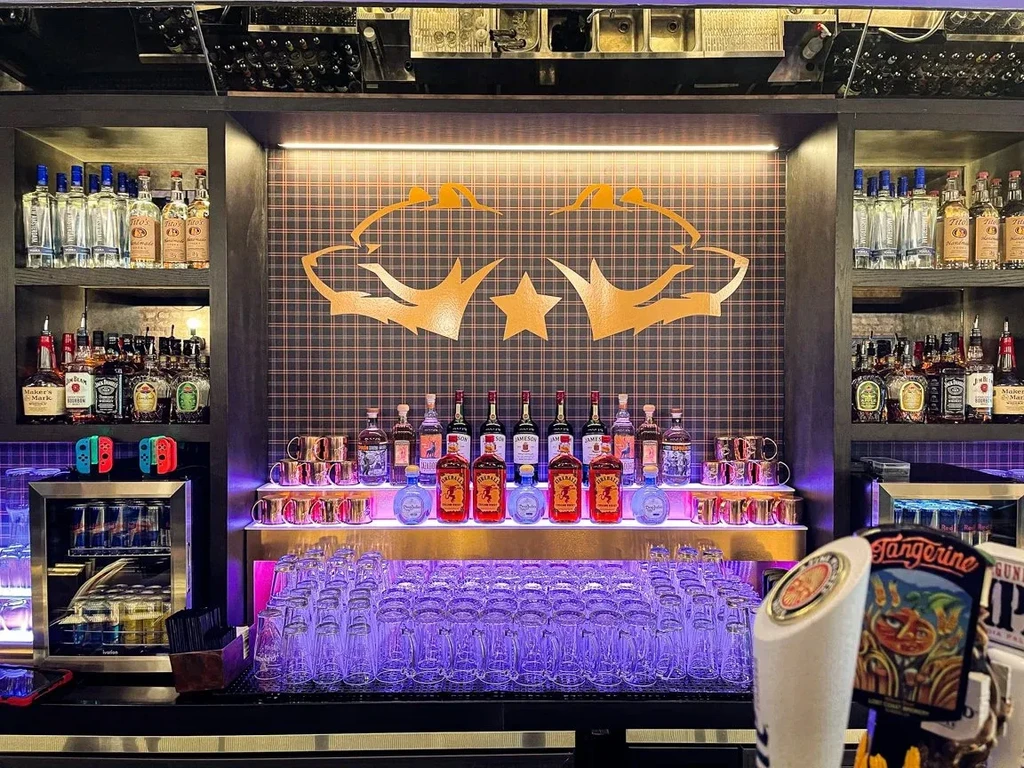 A well-stocked bar with liquor bottles, glassware, and purple lighting.