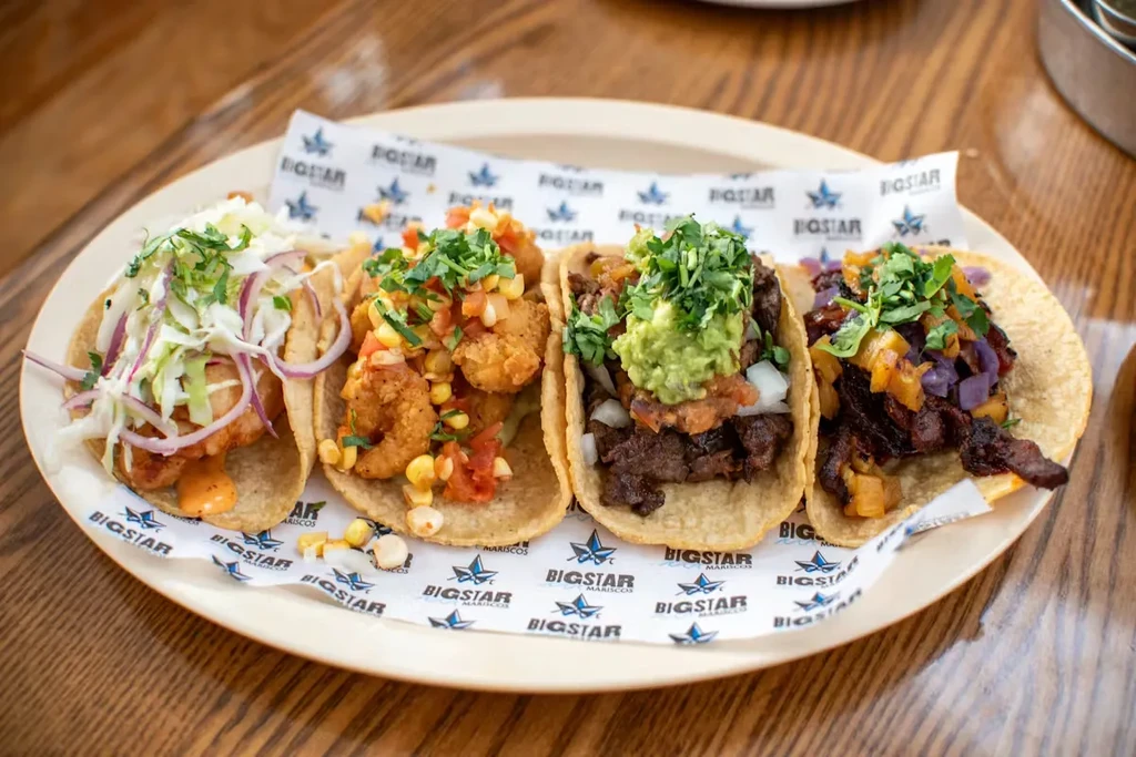 Four diverse tacos arranged on a plate with "BIGSTAR MARISCOS" paper.