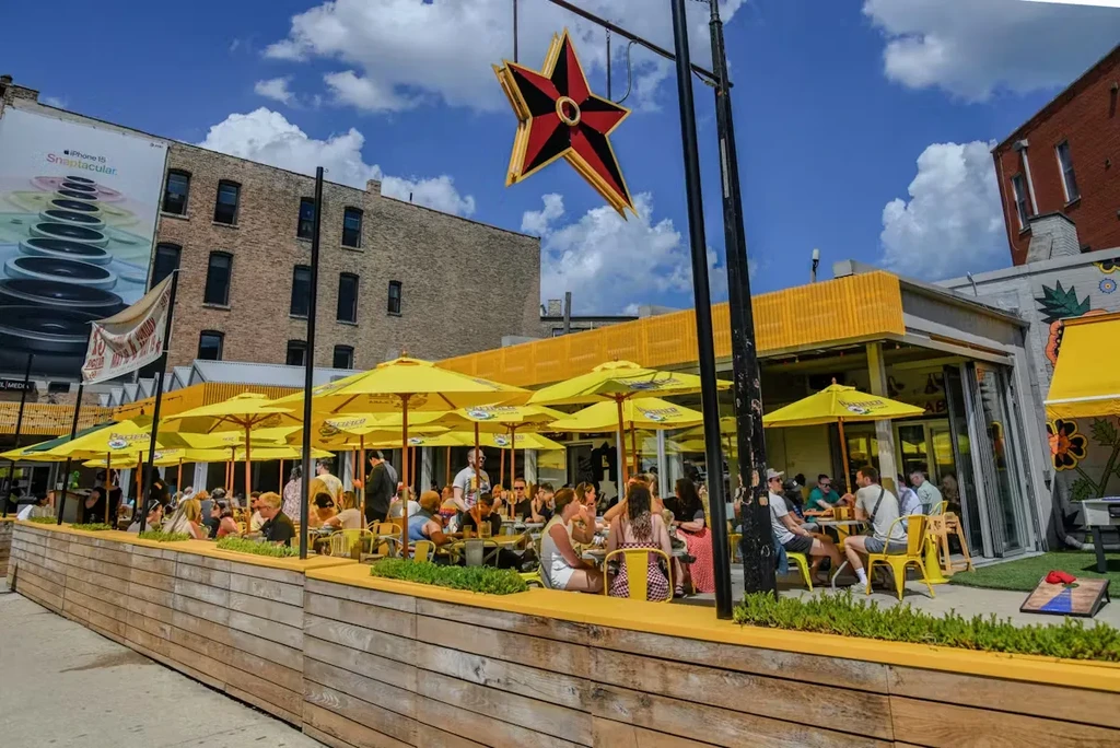 Yellow patio umbrellas shade a restaurant with people dining outdoors.