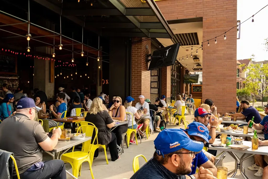 Restaurant patio with people dining, string lights, and yellow chairs.