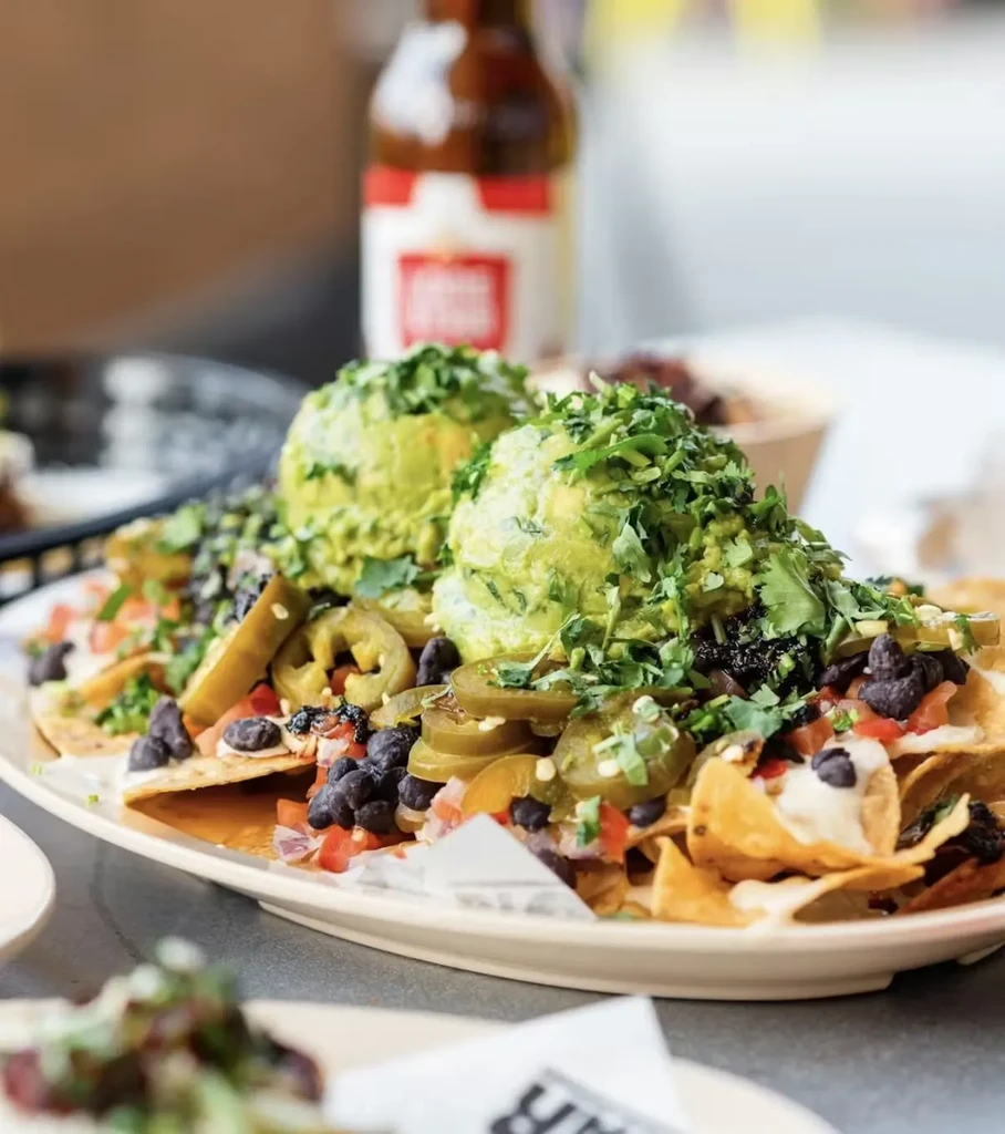 Large plate of nachos with guacamole, jalapeños, beans, and pico de gallo.