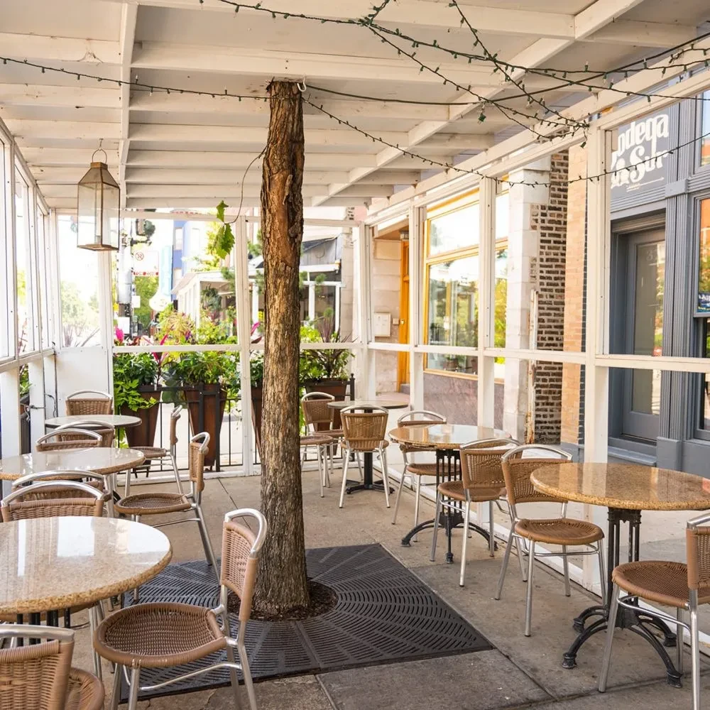 Outdoor patio dining area with round tables, chairs, and a tree.