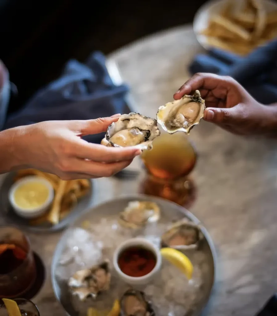 Two hands hold up a fresh oyster in its half shell.