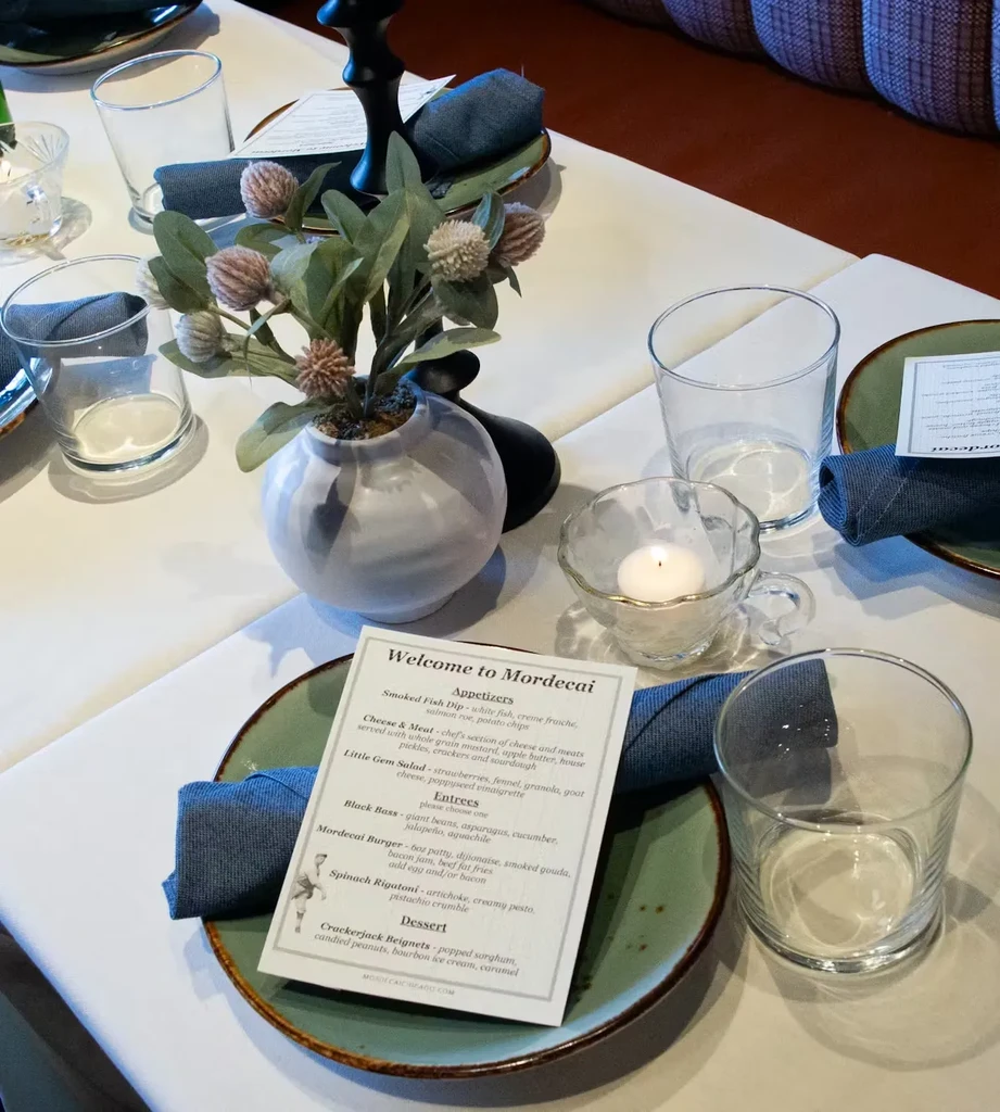 Well-set restaurant table with floral centerpiece, menu, and lit candle.