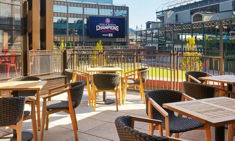 Outdoor patio with tables and chairs overlooking a stadium.