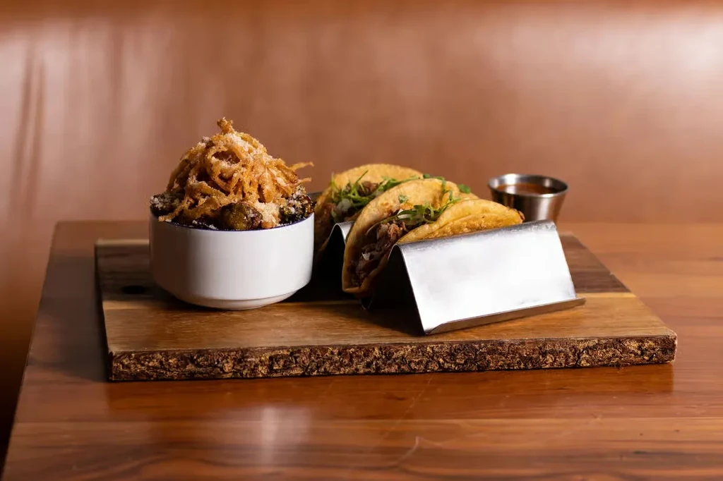 Roasted Brussels sprouts, two tacos, and sauce on a wooden board.
