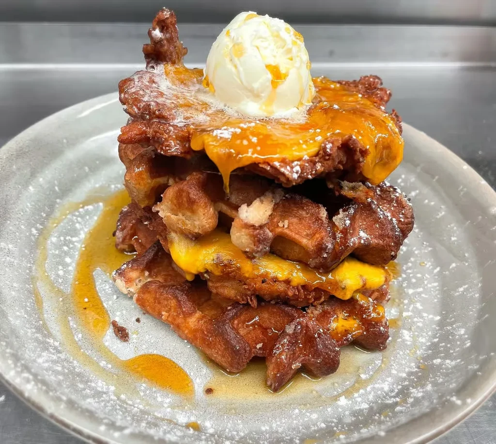 Stack of pastries topped with ice cream, syrup, and powdered sugar.