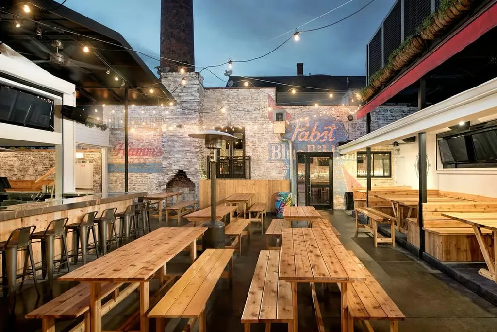 Outdoor restaurant patio with picnic tables, bar, and brick walls.