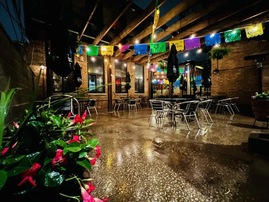 Empty restaurant patio at night with string lights and wet ground.