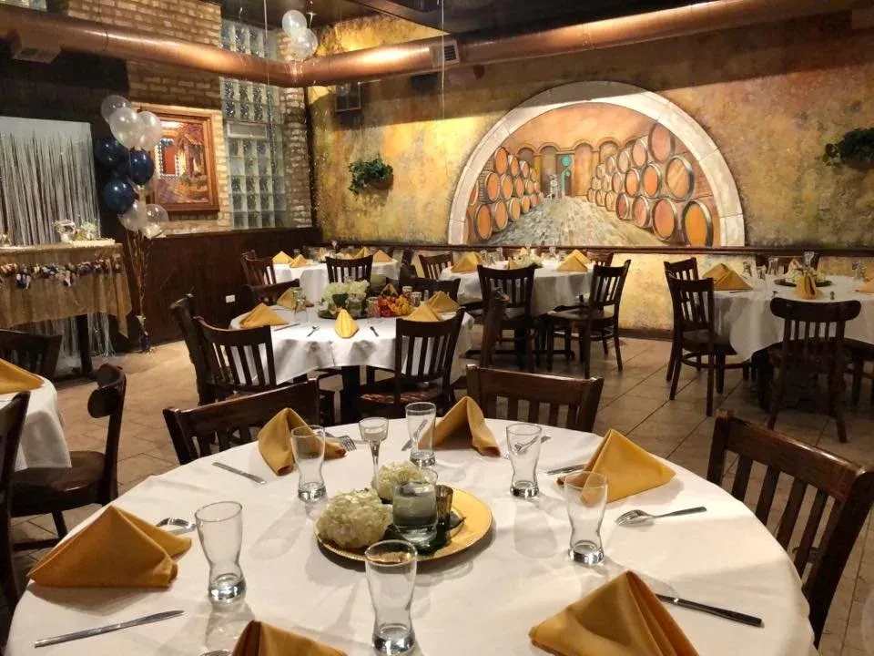 Restaurant interior with round tables, yellow napkins, and wine cellar mural.