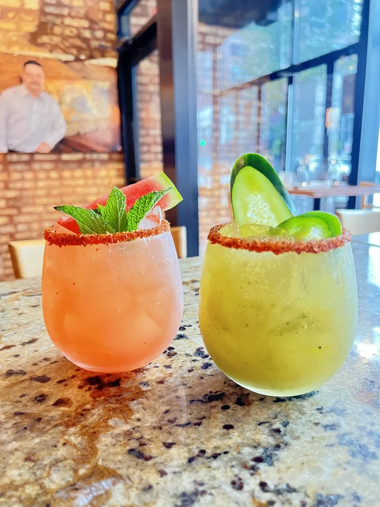 Colorful cocktails on a counter, with a brick wall background.