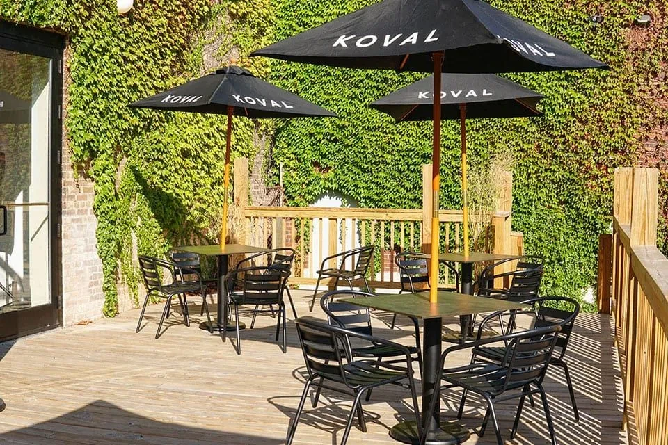 Patio with black tables, chairs, and "KOVAL" umbrellas.